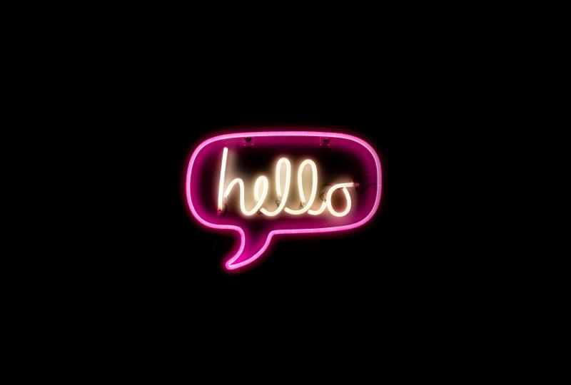 Das Bild zeigt eine Sprechblase in Neonfarben vor schwarzem Hintergrund mit der Aufschrift "hello".